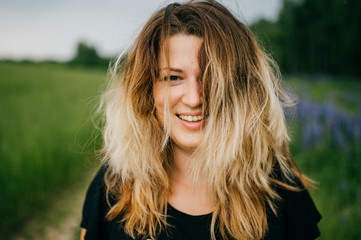 Closeup portrait of young happy smiling mother. Woman with lush long hair cover her face. Half-visible.  Girl outdoor at nature alone with abstract background in wild terrain in summer evening.