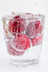 Group of sweet ripe cherries and bubbles of carbon dioxide in a glass of sparkling soda water placed on white background.