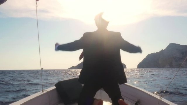 Happy man in suit with a briefcase exulting on the prow of a boat in the middle of the ocean
