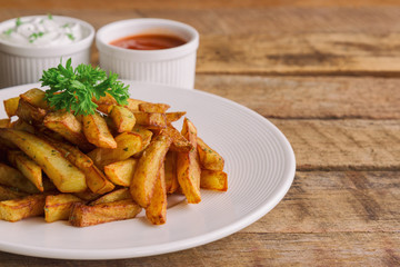 Homemade french fries serve with ketchup and sour cream or mayonnaise. Golden brown crispy french fries sprinkle with salt and oregano on white plate for snack or appetizer.French fries on wood table.
