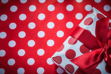 Wrapped gift box with bow on polka-dot red table cloth holidays 
