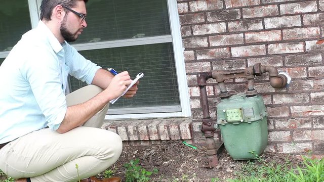 Young millennial home inspector examines gas meter outside a residential home