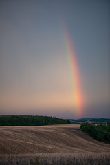 Naklejka na ściany i meble Rainbow over hills. Agricultural fields after sunset with colourful rainbow.