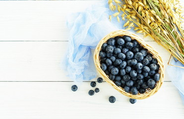 Fresh blueberries and ripe oat spikelets close-up on white wooden background. Top view. Copy space