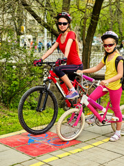 Family bike ride. Mother and daughter wearing bicycle helmet with rucksack. Children biking on yellow bike lane Child in foreground teenager on background Friendship between children of different ages