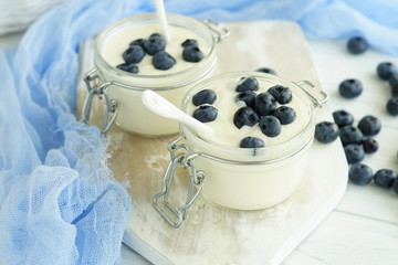 A tasty and healthy breakfast of fresh yogurt with blueberries in a small glass jar on a white wooden background.
