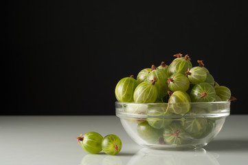 Juicy ripe berries of a gooseberry in a small glass plate on black surface. Gooseberry harvest