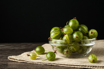 Juicy ripe berries of a gooseberry in a small glass plate on black surface. Gooseberry harvest