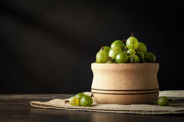 Juicy ripe berries of a gooseberry in a small wooden pot on black surface. Gooseberry harvest
