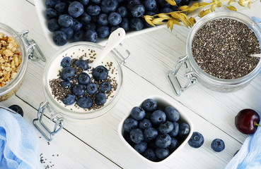 A tasty and healthy breakfast of fresh blueberries, granules, chia seeds, yogurt with blueberries in a glass small jar on a white wooden background.