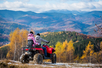 Rear view of man and woman in winter clothing riding a quad bike atv at the hill on the background of beautiful landscape mountains and forests.