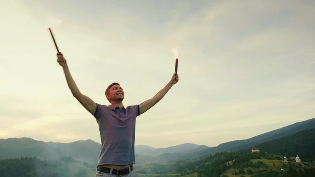 A man in the mountains signals with hand fireworks, looks up. Concept distress signal, need help