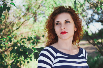 Fototapeta premium Beautiful red-haired girl. Gentle portrait of a young attractive woman. Girl with a pensive look on a natural background among the trees.