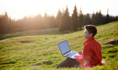 Rearview shot of a woman relaxing on the grass using her laptop copyspace sunlight evening blissful...
