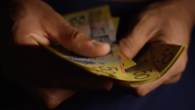 Male hands counting a wad of Australian dollars, in dramatic lighting