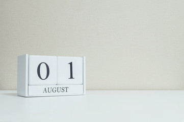 Closeup white wooden calendar with black 1 august word on blurred white wood desk and cream color wallpaper in room textured background with copy space , selective focus at the calendar