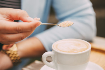 Close-up of a spoon in a female hand pouring sugar into her coffee cup