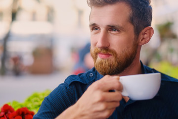 A man drinks coffee in a cafe on a street.