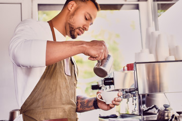 Black bearded coffee seller pouring coffee.