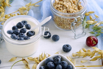 A tasty and healthy breakfast of granules, yogurt with blueberries in a glass small jar on a white wooden background.