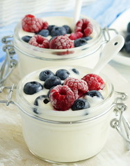 A tasty and healthy breakfast of fresh yogurt with blueberries and raspberries in a small glass jar on a white wooden background.Close up