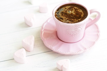 Pink cup with coffee and marshmallows hearts on a white wooden background