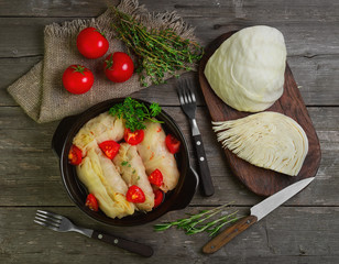 Cabbage rolls with meat and rice in bowl. Fresh cut cabbage and cherry tomatoes, greenery for cooking cabbage rolls with meat. Cabbage rolls on gray wooden rustic background. Top view, flat lay.