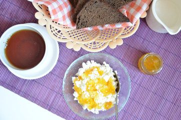 Breakfast on the table cup with tea milkwoman rye bread curds orange jam on a purple napkin
