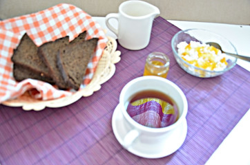 Breakfast on the table cup with tea milkwoman rye bread curds orange jam on a purple napkin