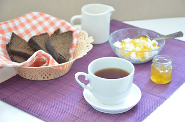 Breakfast on the table cup with tea milkwoman rye bread curds orange jam on a purple napkin