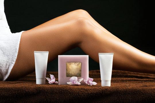 Pr&eacute;sentation de tubes de cr&egrave;me et d'une bougie devant les jambes bronz&eacute;e d'une femme