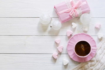 Fototapeta na wymiar Pink cup with coffee, marshmallows hearts, Christmas balls and gift on a white wooden background.Top view. Copy space