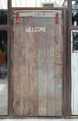 Welcome sign written by chalk on wood door background.