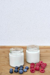 Yogurt in glass jar, raspberries and blueberries on a wooden background - vertical