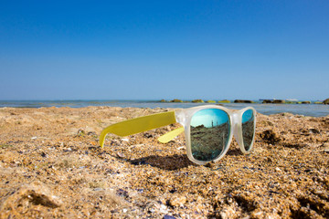 Poly-color sunglasses, reflecting the ocean and a shell on a sandy, beach