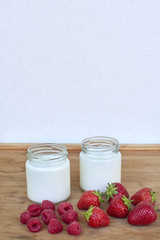 Yogurt in glass jar, raspberries and strawberries on a wooden background - vertical