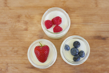 Three glass jars with yogurt on a wooden background - directly above