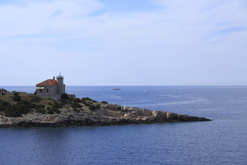 Island with small house on rocks, Photo of small island with boats and blue sea in the background