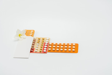 Pile of birth control pills with flower on white background