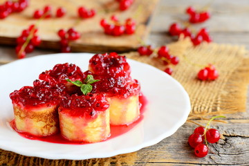 Fried pancakes with redcurrant sauce. Homemade pancakes sushi on a white plate and a vintage wooden table. Beautiful and healthy breakfast for kids and whole family