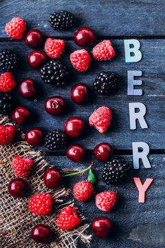 Summer and Autumn fresh berries on blue wooden table background. Top view delicious Vegetarian food - raspberry, blackberry, cherry. Wooden letters word - plum