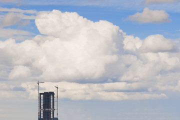 A high-rise building under construction against a background of a fluffy cumulus cloud. Stairway to Heaven. Modern Tower of Babel.
