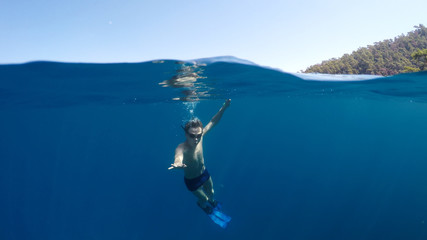 Half underwater close up, swimmer in flippers dives into the sea