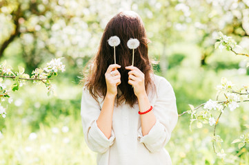 Unrecognizable unknown brunette scarecro with hidden face standing in emerald blooming garden. Teenager holding two dandelions in front of eyes. Chewbacca and chupacabra funny style imitation. Fooling