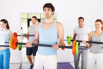 Group of people lifting barbells in weight training class.