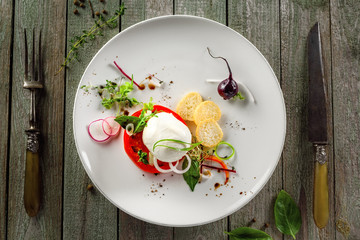 Caprese salad made of fresh mozzarella, tomato and herbs on a table. Italian healthy food on a plate. Top view.