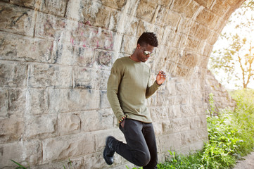 Handsome young african american guy in casual clothing and sunglasses posing and walking in the...