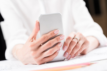 cropped shot of woman with beautiful french manicure using smartphone