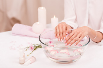 cropped shot of woman receiving spa treatment for hands in glass bowl with rose petals