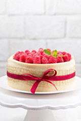 Birthday spongecake with raspberries decorated red ribbon and bow on a white cake stand